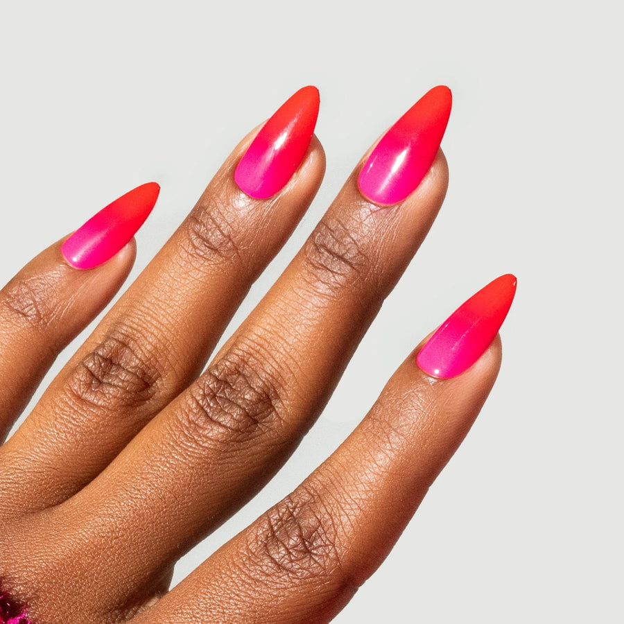 Close-up of hands with bright pink nail polish wearing red fuzzy gloves on a light gray background