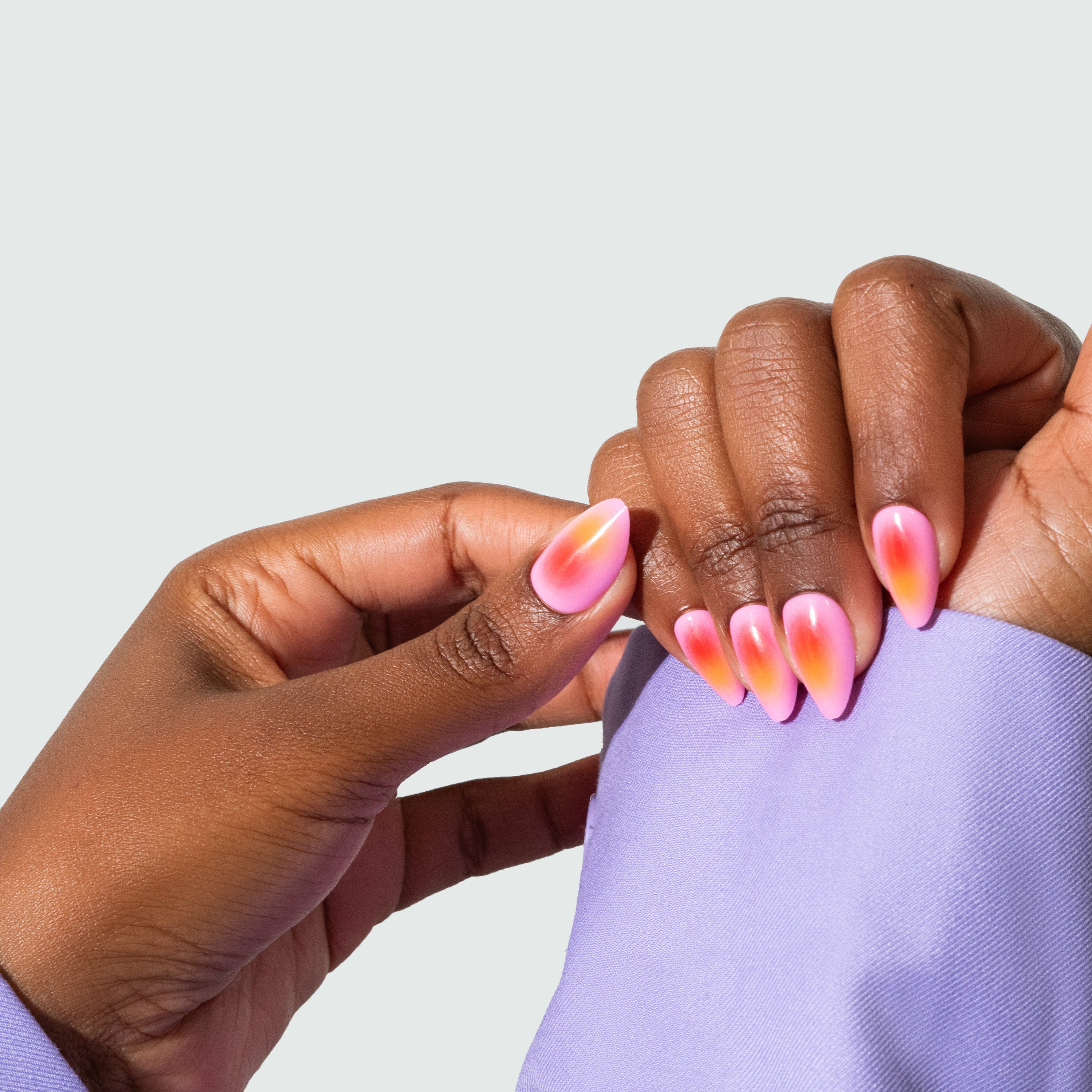 A pair of press-on nails with a gradient design in pink, orange, and yellow hues, being worn on an arm.