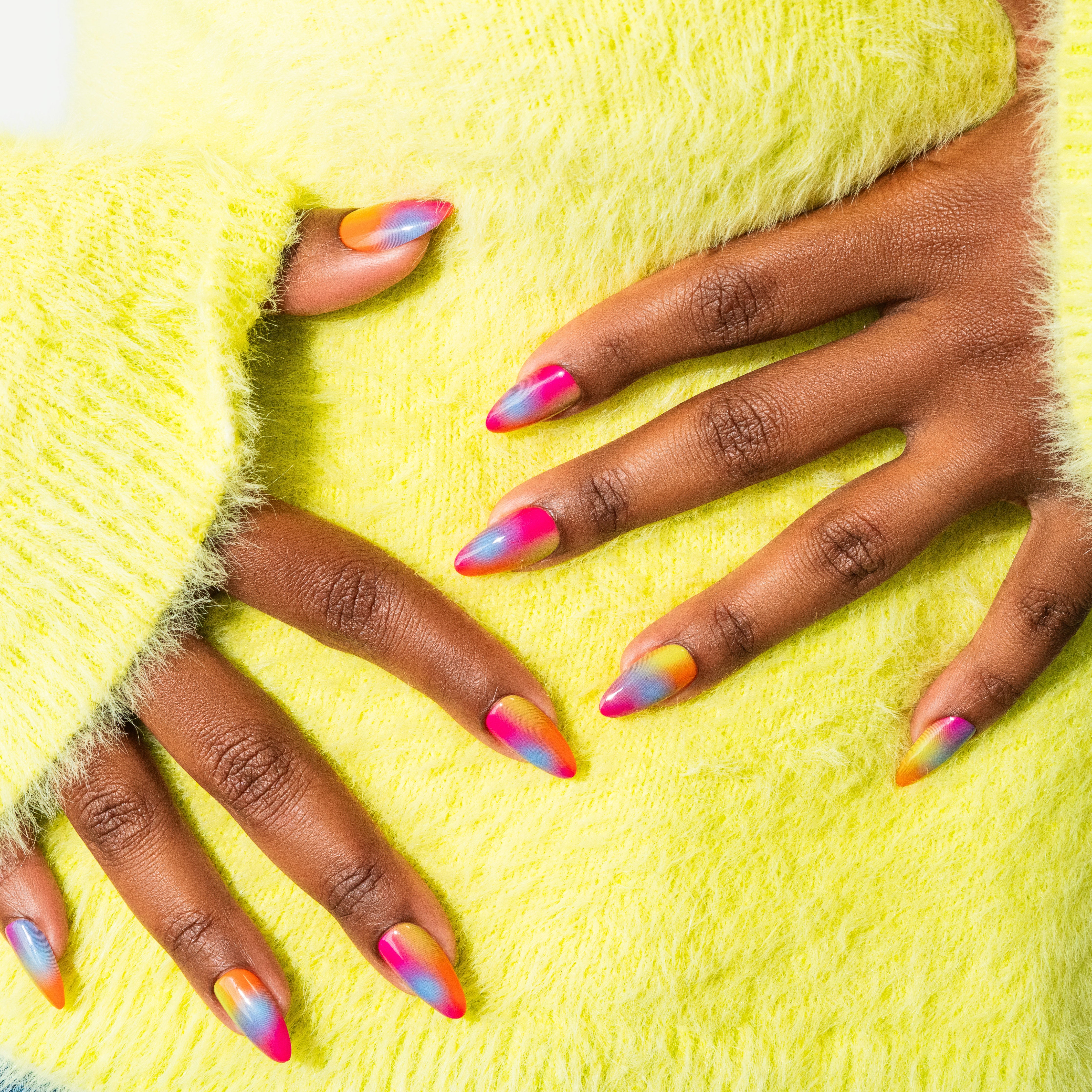 A set of press-on nails featuring a gradient of warm colors, resembling a tropical sunset, on a person's hands.