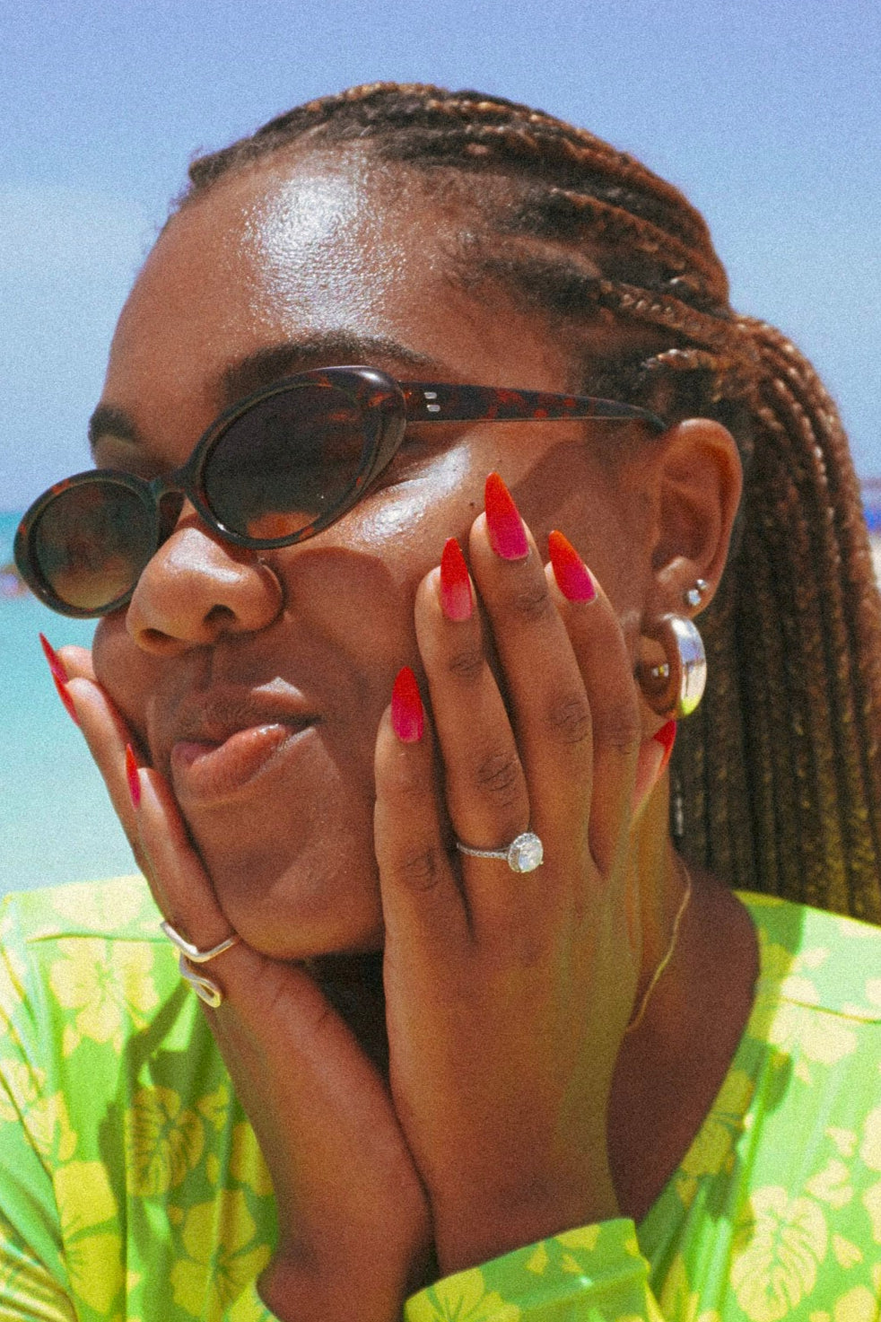 Woman in a green dress with sunglasses and red nails on a beach