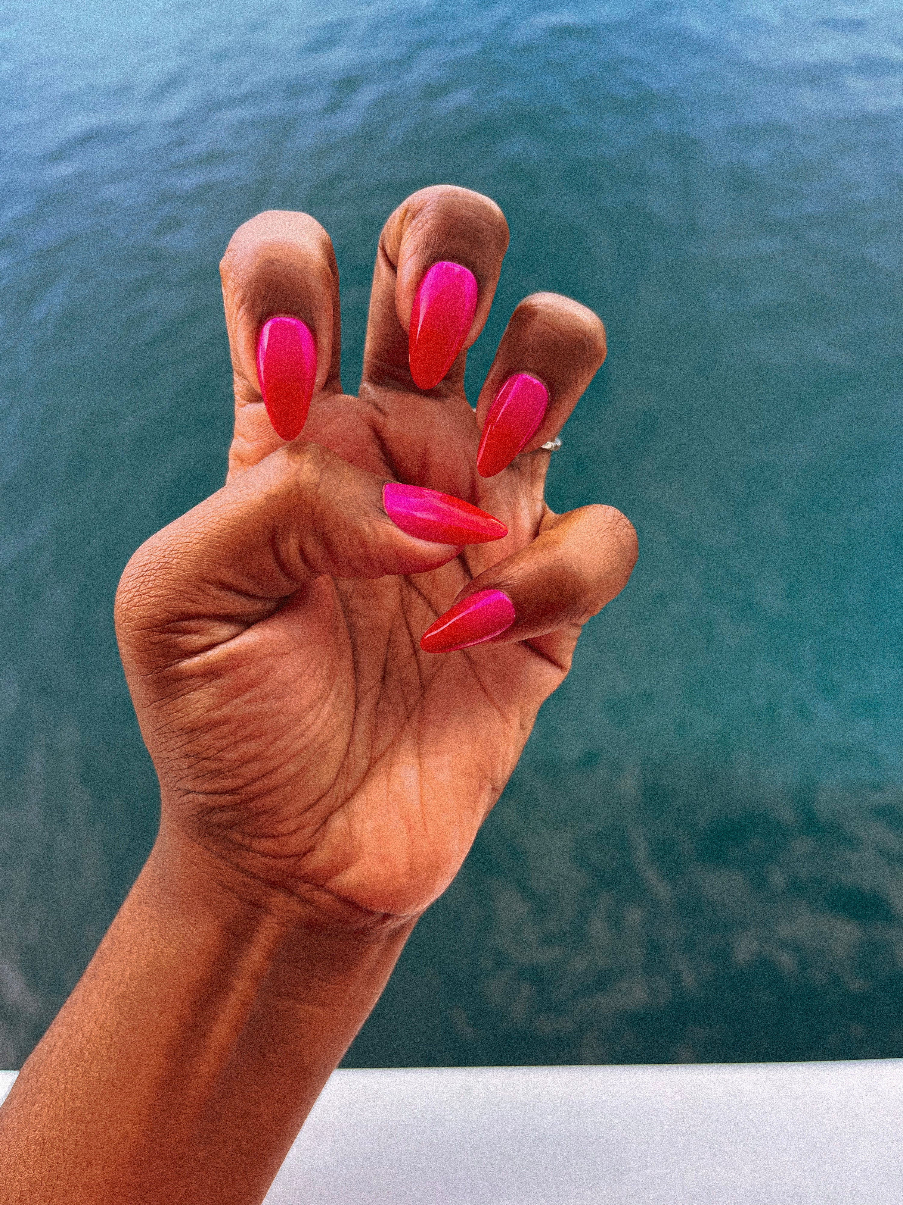 Hand with pink press-on nails against a blurred water background