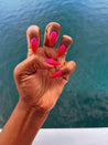 Hand with pink press-on nails against a blurred water background
