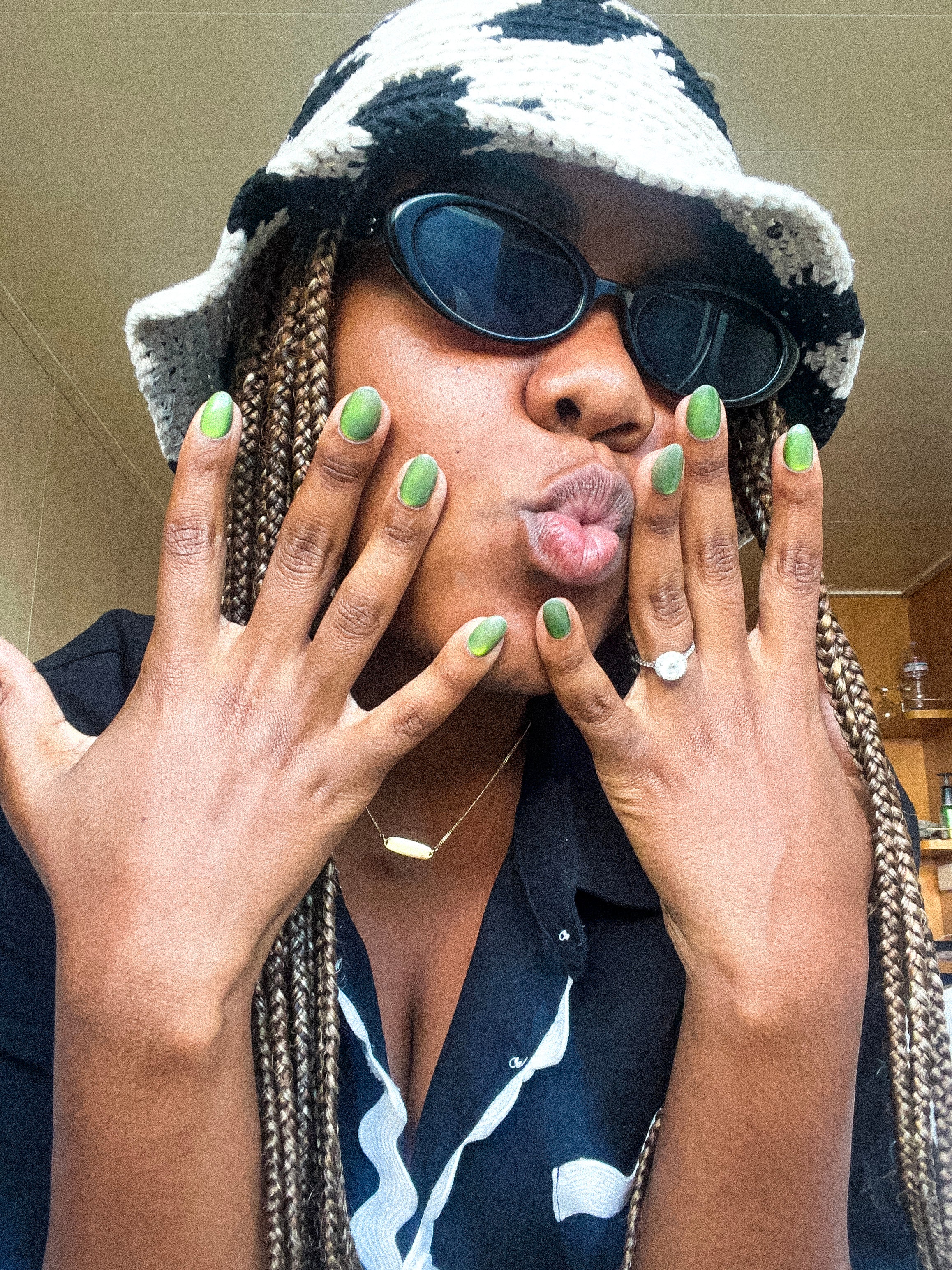 Person wearing a black and white hat, sunglasses, and dark clothing with green nail polish press on nials